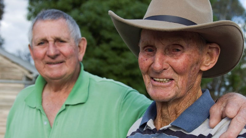 Senior men outdoors with hand over shoulder smiling at camera